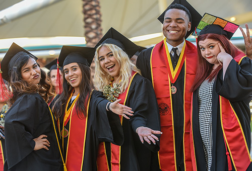 5 graduates celebrating in their cap and gowns