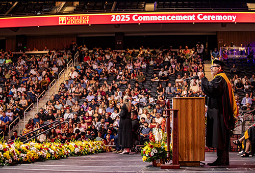 Photo of a commencement ceremony with someone at the podium addressing the graduates and crowd