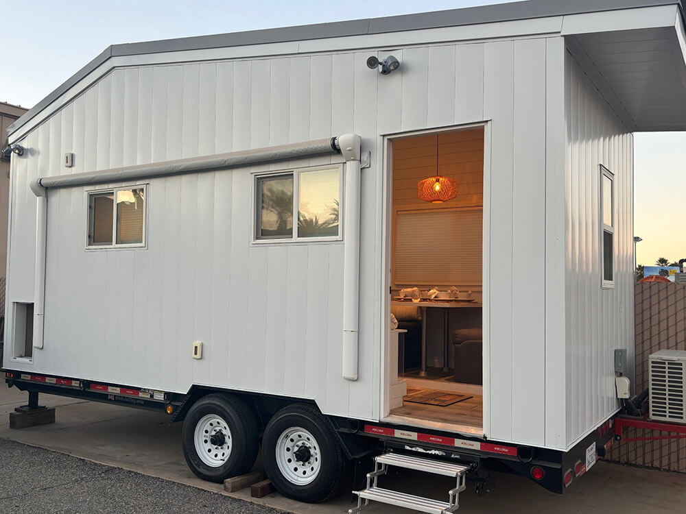 tiny-home-01_1000_opt Photo showing the outside of the Tiny Home with the door open and a light on inside.